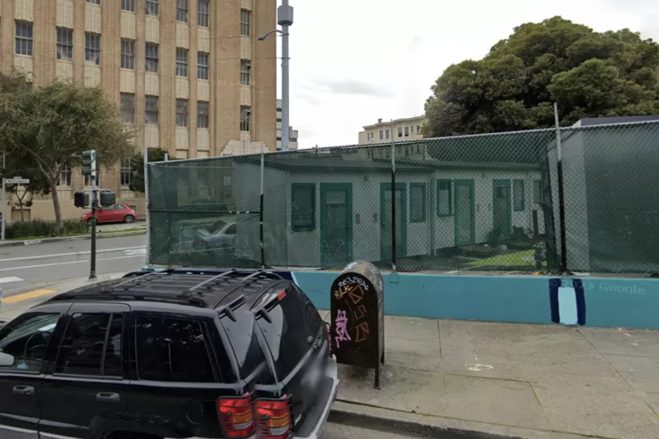 Google street view of tiny home village behind see-through green fence at 33 Gough St. in San Francisco with brick building in background